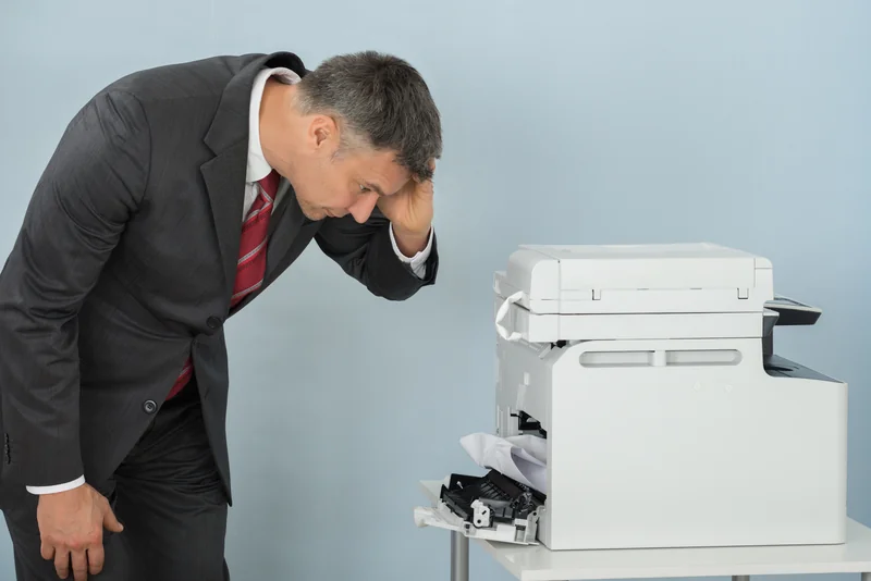 Frustrated office worker looking at a jammed copier with the front panel open